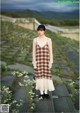 A woman in a plaid dress standing in a field of flowers.