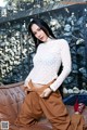 A woman in a white top and brown pants posing on a brown couch.