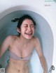 A woman in a bathtub laughing in the water.