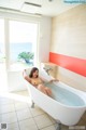 A woman sitting in a bathtub in a bathroom next to the ocean.