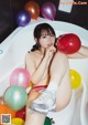 A woman sitting in a bathtub surrounded by balloons.