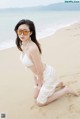 A woman in a white bikini sitting on the beach.