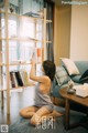 A woman sitting on the floor in front of a book shelf.