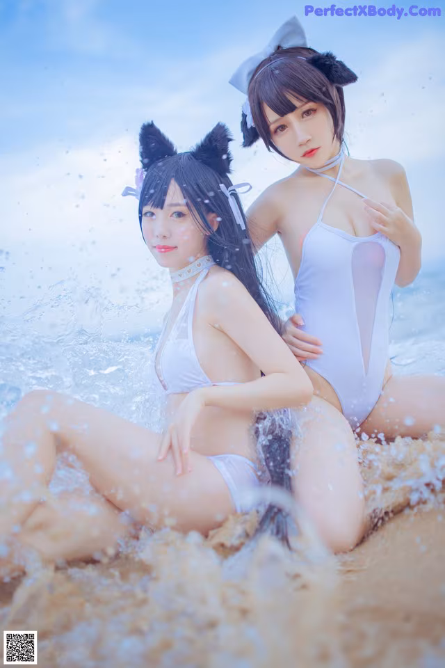 Two women in white bathing suits sitting in the water.