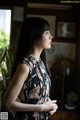 A woman in a floral dress standing in front of a window.