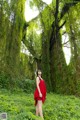 A woman in a red dress standing in the middle of a forest.