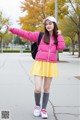 A woman in a pink jacket and yellow skirt holding a cup of coffee.