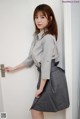 a woman in a gray shirt and skirt leaning against a door