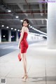 A woman in a red dress standing in a parking garage.